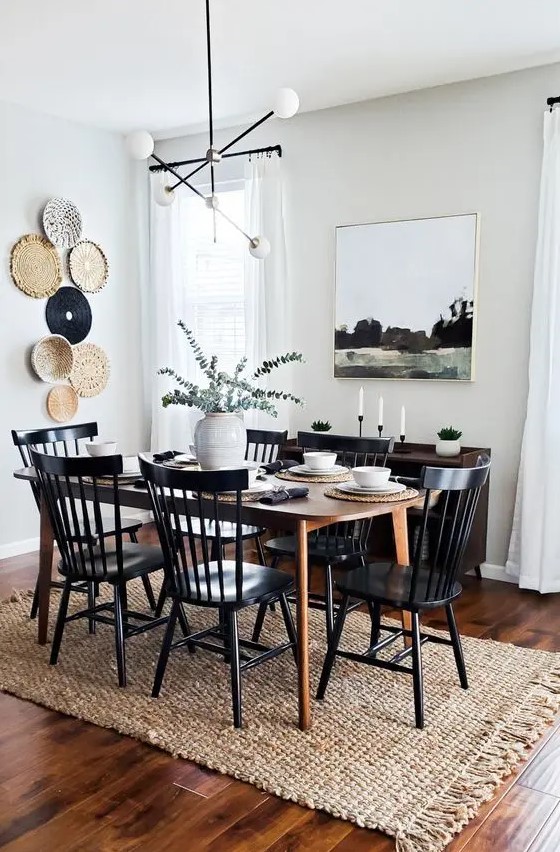 a modern farmhouse meets boho dining room with a stained table, a dark-stained credenza, black chairs, a gallery wall of plates and an artwork