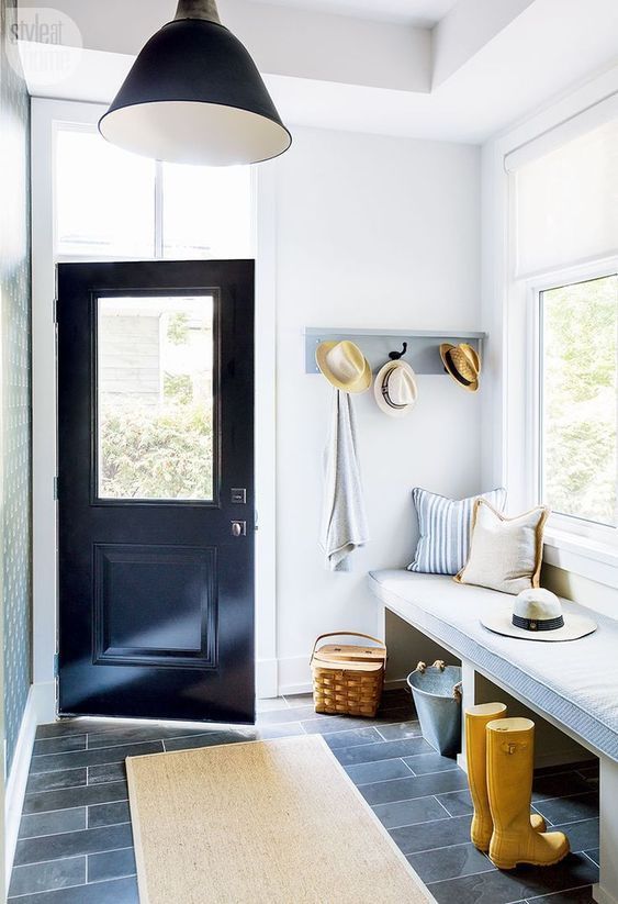 a modern farmhouse mudroom with a bench with a cushion and pillows, a racj, a basket, a rug and a black pendant lamp
