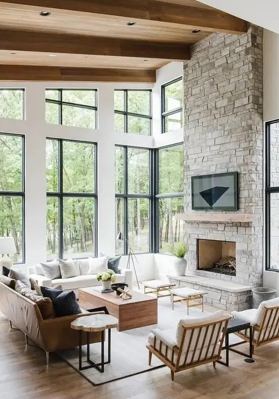 a modern farmhouse style living room with a fireplace clad with stone, chic neutral furniture, stools and coffee tables