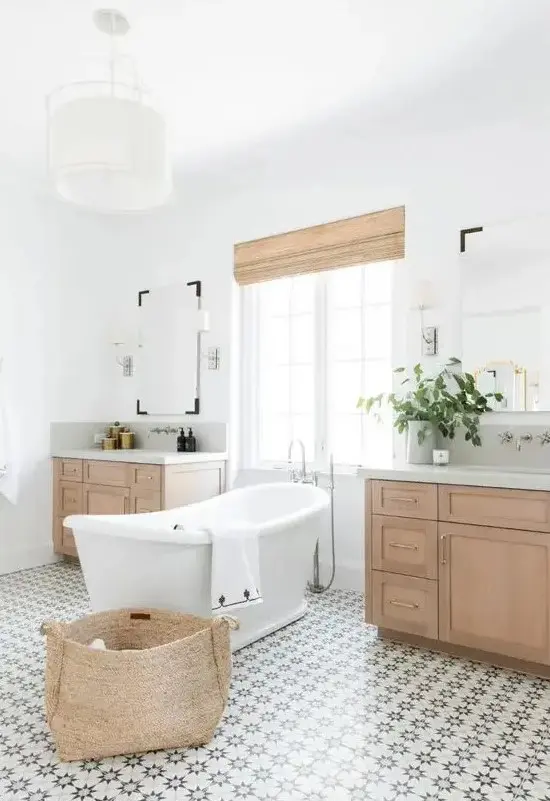 a modern rustic bathroom with a lovely patterned tile floor, stained vanities, a basket and shades plus a vintage inspired tub