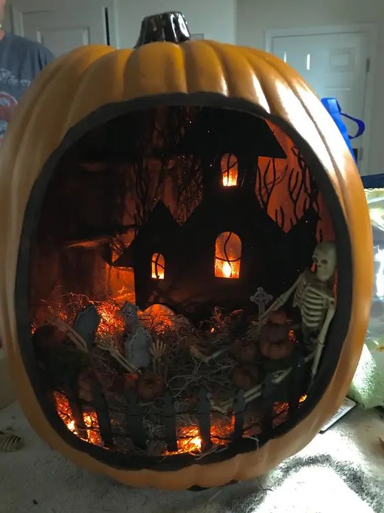 a moody Halloween diorama with a graveyard, lights, a black house and a skeleton plus little pumpkins is a bold idea