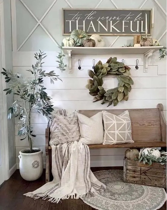 a neutral farmhouse entryway with a leaf wreath, a potted tree, faux pumpkins, candles and neutral textiles