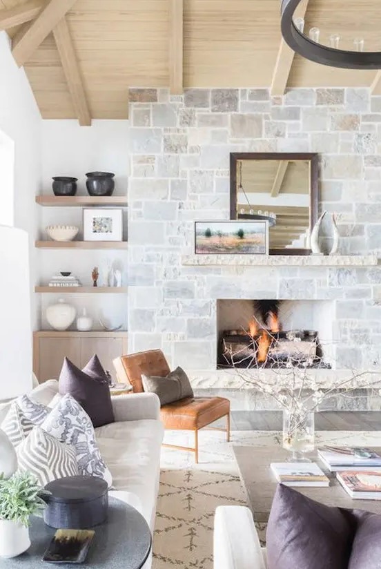 a neutral farmhouse living room with a stone fireplace, a wooden mantel, artworks and a mirror that becomes a centerpiece here