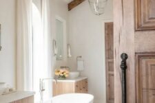 a neutral modern farmhouse bathroom with fluted floating vanities, an oval tub, a tiled floor and stained wooden beams