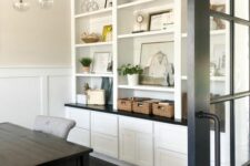 a neutral modern farmhouse home office with built-in storage units, a black desk, a grey chair, a black chandelier