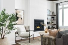 a neutral modern farmhouse living room with a built-in fireplace, dark-stained shelves, a taupe sofa, white chairs and a round coffee table