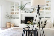 a neutral modern farmhouse living room with a fireplace, built-in shelves, a neutral sofa with pillows, a black side table and a floor lamp