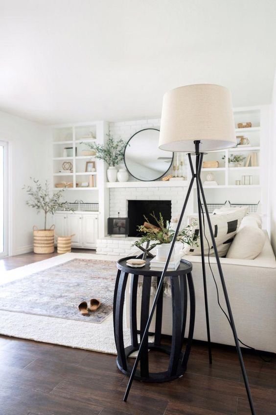 a neutral modern farmhouse living room with a fireplace, built-in shelves, a neutral sofa with pillows, a black side table and a floor lamp