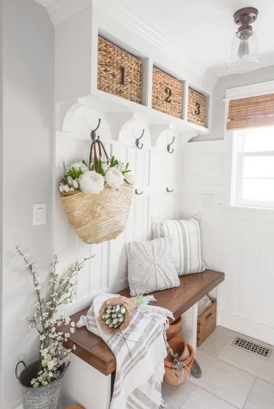 a neutral modern farmhouse mudroom with a built-in bench and baskets, lots of blooms and greeneyr, some pillows