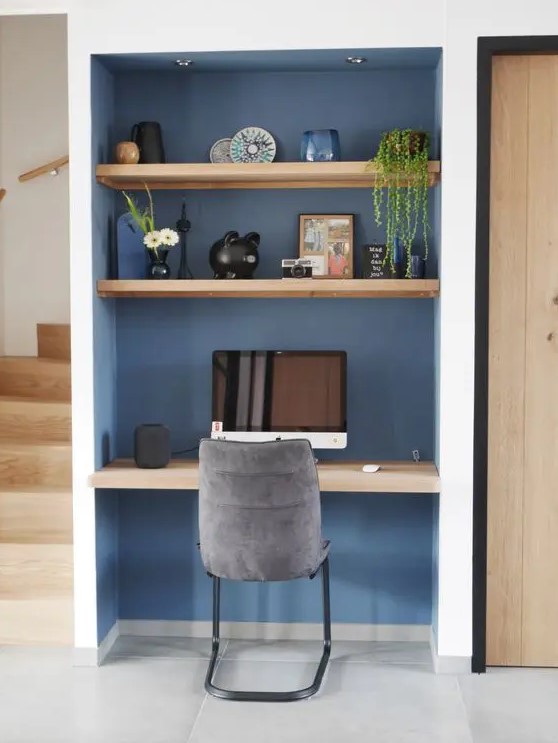 a niche painted blue with built-in shelves and a desk, some lovely decor, a PC and a grey chair is a cool solution
