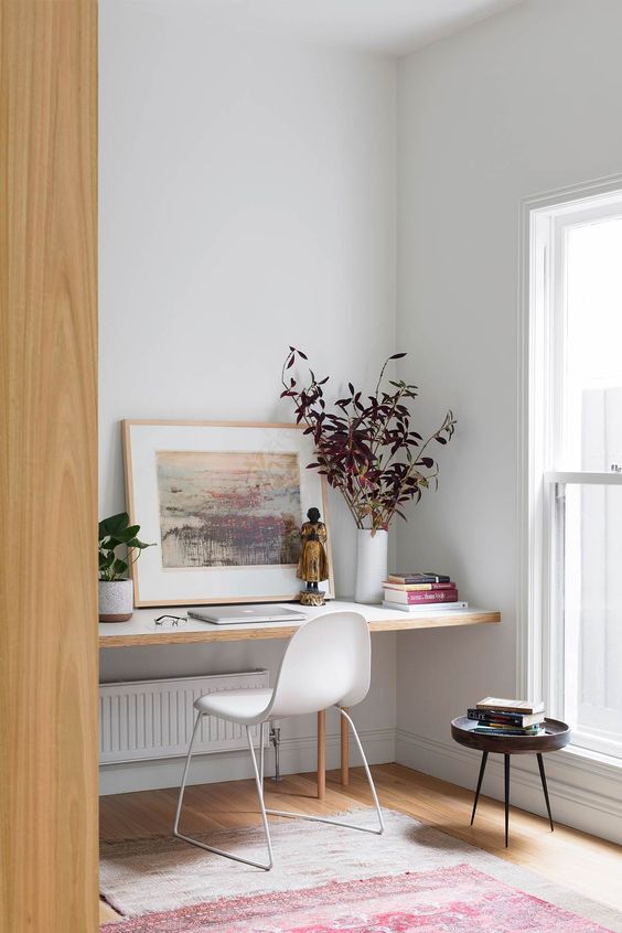 a niche with a built-in desk, some plants, an artwork and books, a modern white chair is a cool nook for working