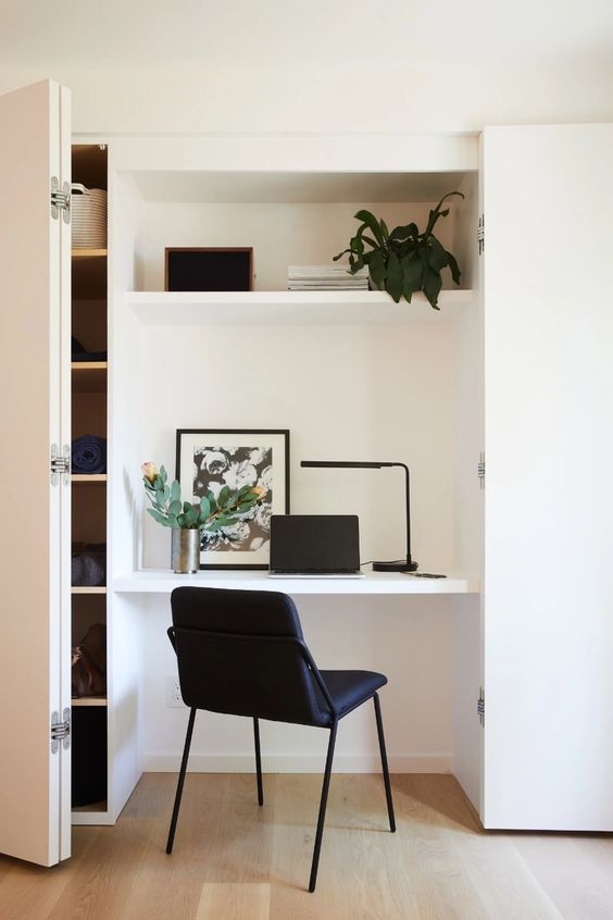 a niche with a small home office, a built in shelf and a desk, a black chair, some decor and a stylish table lamp