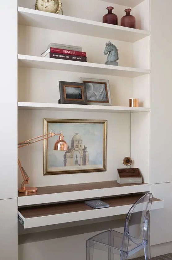 a niche with built-in shelves and a desk plus a retracting part, books, artwork, vases and a copper table lamp