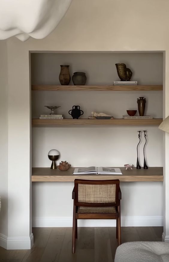 a niche with built-in wooden shelves and a desk, some chic decor, vases and books and a mid-century modern chair
