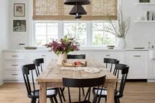 a pretty modern farmhouse dining space with white cabinetry, a stained dining table and black chairs, black pendant lamps and some art