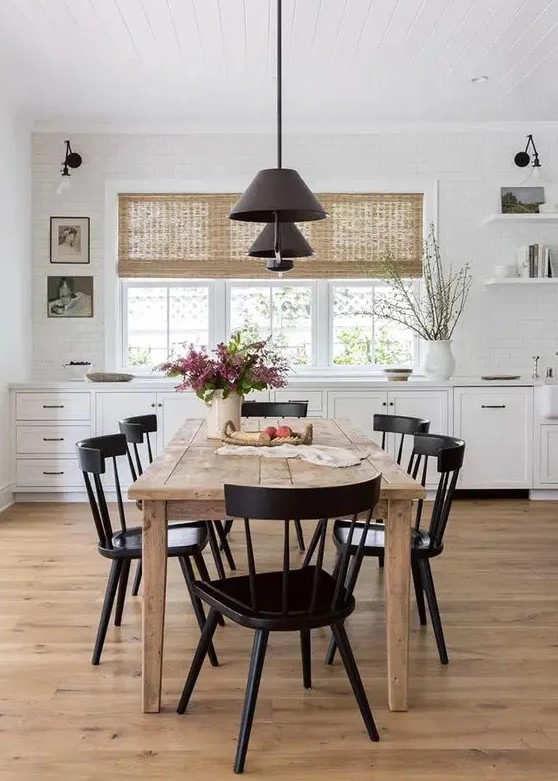 a pretty modern farmhouse dining space with white cabinetry, a stained dining table and black chairs, black pendant lamps and some art