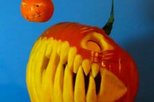 a scary angler fish pumpkin with giant teeth and a mini pumpkin hanging is jaw-dropping for Halloween