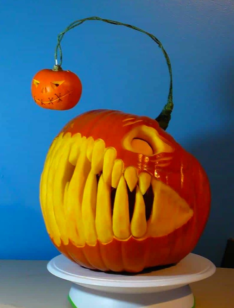 A scary angler fish pumpkin with giant teeth and a mini pumpkin hanging is jaw dropping for Halloween