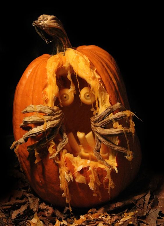 a scary carved Halloween pumpkin with eyes, teeth and monster hands is a bold and cool idea for Halloween