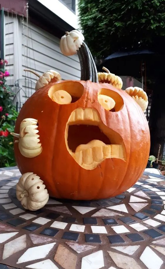 a scary carved pumpkin being eaten by other mini pumpkins is a very fun and spooky idea to realize for Halloween