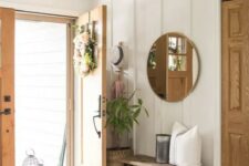 a simple and stylish modern farmhouse entryway with a bench, some baskets, a round mirror and some greenery