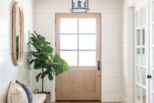 a simple modern farmhouse entry with shiplap walls, an upholstered bench, a tree in a basket, a mirror and a pendant lamp