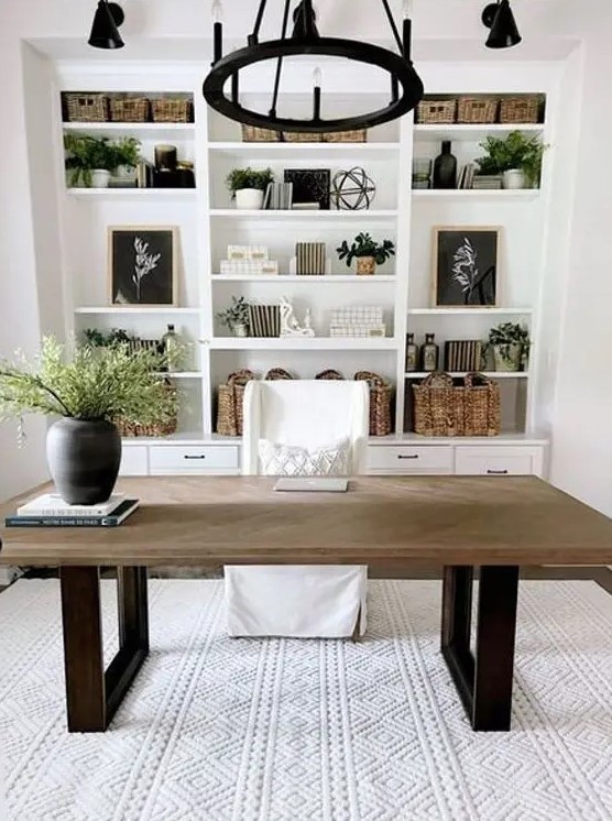 a simple modern farmhouse home office with a large white built in storage unit, a heavy desk, a white chair, a black chandelier