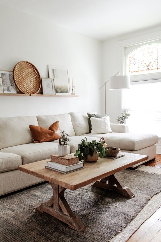 a simple neutral living room with a creamy sofa, a stained coffee table, a ledge gallery wall and some greenery