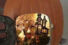 a small Halloween pumpkin diorama with a black painted house, a black tree with lights, moss, pumpkins and bats