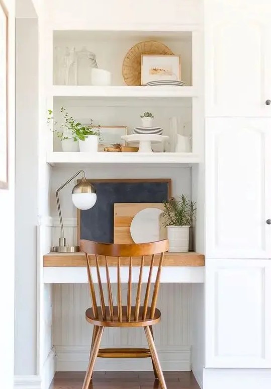 a small nook with a built in working space   a desk, a couple of shelves, potted greeneyr and some cutting boards can be located in the kitchen
