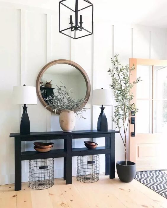 a stylish modern farmhouse entryway with a black console table, wire baskets, a mirror in a wooden frame, a potted plant and table lamps