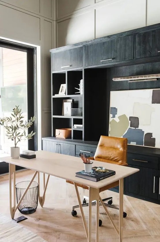 a stylish modern farmhouse home office with a black storage unit, a lightweight desk, an amber leather chair and some art