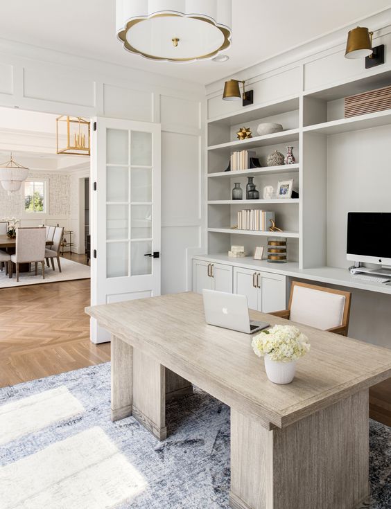 a stylish modern farmhouse home office with built in cabinets, a neutral desk, a wihte chair and a pendant lamp