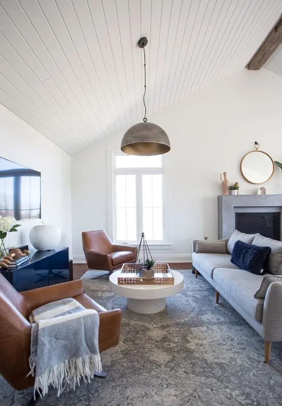 a stylish modern farmhouse living room with a fireplace, a grey sofa, leather chairs, a glossy sideboard and a coffee table