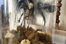 a unique Halloween cloche with moss, white pumpkins, a skeleton with black feather wings is a gorgeous idea