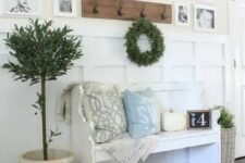 a welcoming farmhouse entryway with a gallery wall of family pics, a white bench with pillows, potted plants and a rack