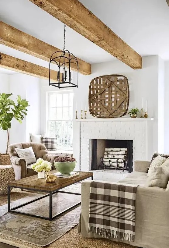 a welcoming modern country living room with a brick clad fireplace, neutral furniture, layered rugs, printed textiles and wooden beams on the ceiling