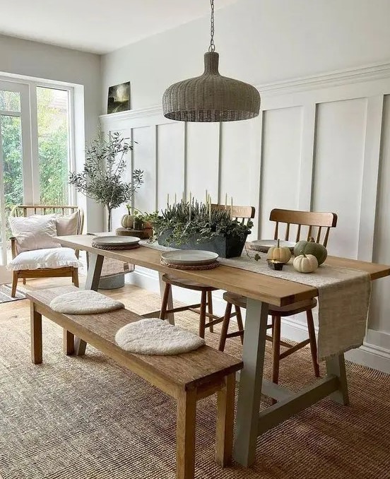 a welcoming neutral dining space with a stained trestle table, bench and chairs, a woven pendant lamp and potted plants