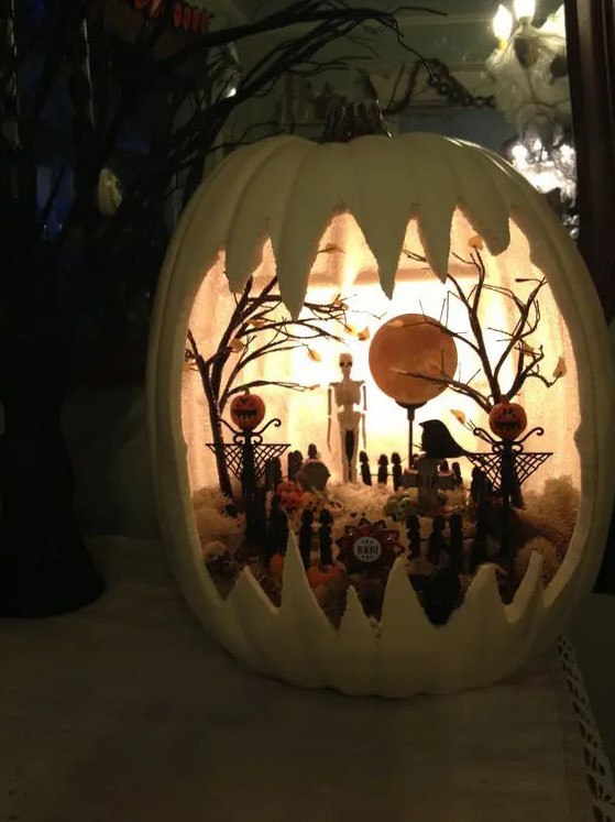 a white Halloween pumpkin diorama with a skeleton, pumpkins, trees, hat and tombstones plus lights is amazing