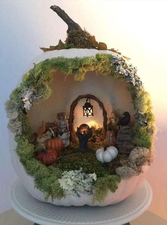 a white Halloween pumpkin with moss, mini pumpkins, a claw paw with a crystal ball and some light is a creative idea