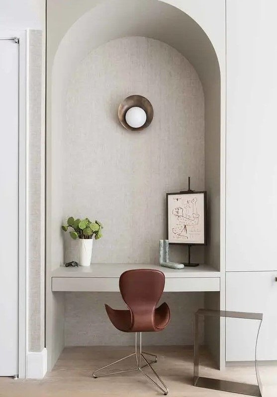 an ached niche with a built in desk, some art, a sconce and a burgundy chair is adorable and chic
