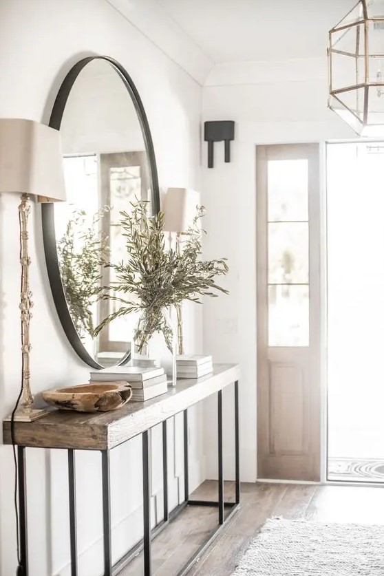 an airy modern farmhouse entryway with a large mirror, a console table, some greenery and table lamps and coffee table books