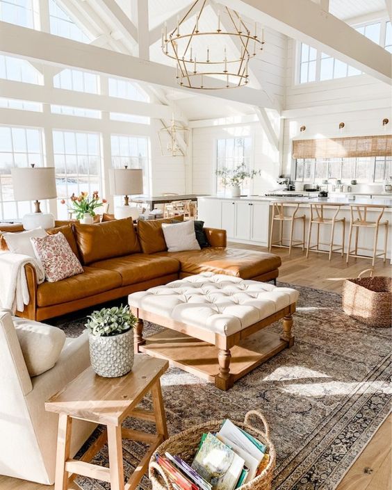 an airy modern farmhouse living room with an amber leather sofa, a neutral ottoman, a creamy chair and baskets