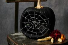 an elegant matte black pumpkin carved, with a spiderweb and a spider plus a gold stem is super chic