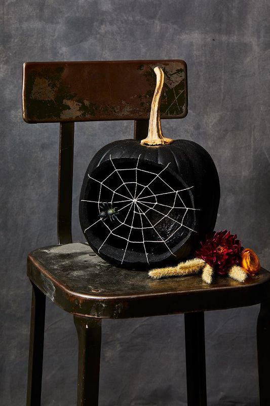 an elegant matte black pumpkin carved, with a spiderweb and a spider plus a gold stem is super chic
