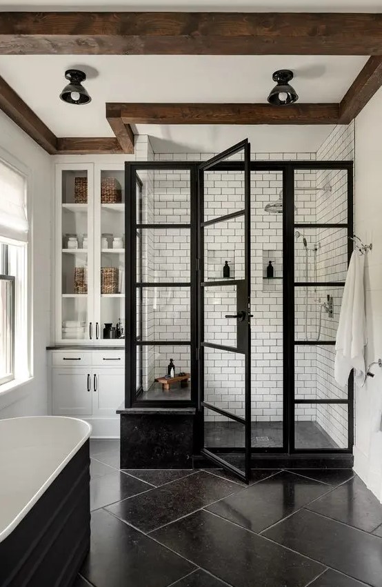 an elegant modern farmhouse bathroom with a shower space done with white subway tiles, a black tub, large scale tiles and a built in storage unit