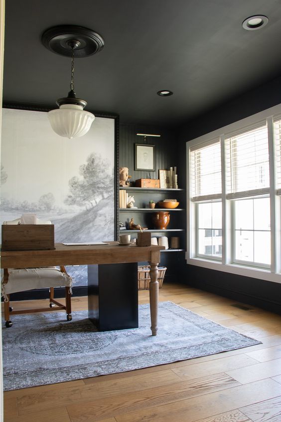 an elegant modern farmhouse home office with a black ceiling and walls, a stained desk and a neutral chair, an oversized artwork and built in shelves