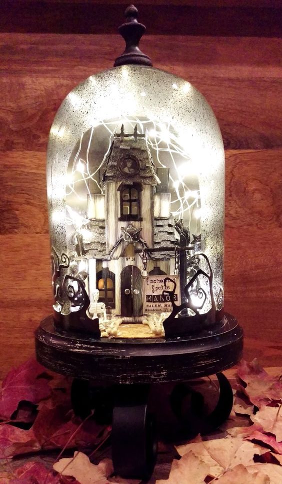 an enchanted Halloween cloche with a haunted house, lights and black trees is a gorgeous decoration