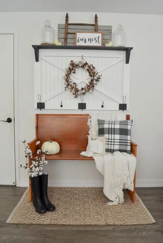 an inviting farmhouse entryway with an amber stained wooden bench, a wooden rack, some decor and artworks