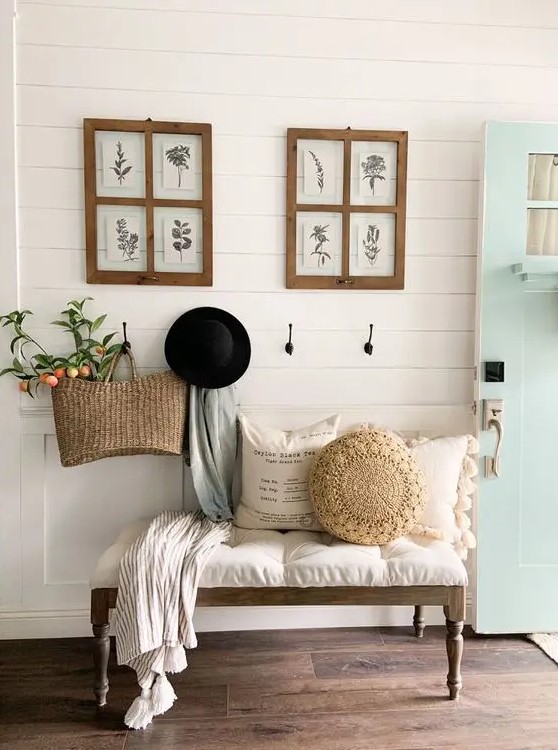 an inviting modern farmhouse entryway with an upholstered bench and pillows, some art, a woven bag with decor